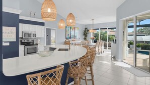 Een moderne keuken met een groot eiland, witte kastjes en een eethoek met rieten stoelen.