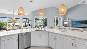 Een moderne keuken met witte kasten, een groot eiland en drie gevlochten hanglampen.