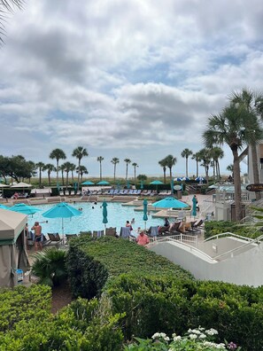 Ein Poolbereich eines Resorts mit mehreren Schwimmbecken, Liegestühlen und Sonnenschirmen.
