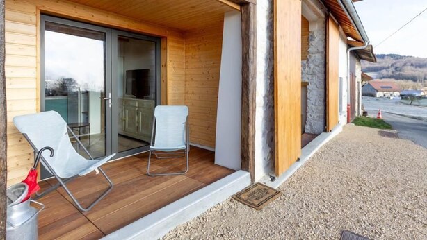 Een houten gevel met een schuifdeur die leidt naar een balkon met twee stoelen.