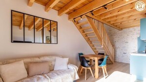 Een gezellige kamer met houten plafond, een bank, een eettafel met stoelen en een trap.