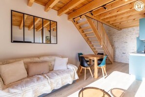 Ein gemütliches Zimmer mit Holzboden, einer Couch, einem Esstisch mit Stühlen und einer Treppe.