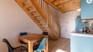 Een houten eettafel met twee stoelen, een keuken met een blauw aanrecht en een houten trap.