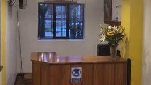 A reception desk with a blue sign, a window with blinds, and a chandelier. - HOTEL HUAYNAPATA PARDO (Cusco)