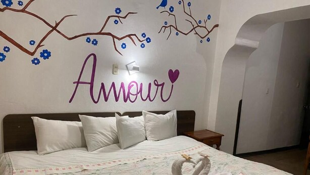 A bedroom with a bed, white pillows, a floral bedspread, and a towel sculpture on the bed. - HOTEL HUAYNAPATA PARDO (Cusco)