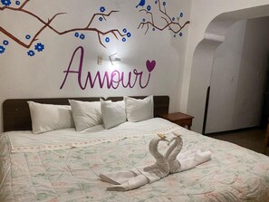 A bedroom with a bed, white pillows, a floral bedspread, and a towel sculpture on the bed. - HOTEL HUAYNAPATA PARDO (Cusco)