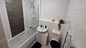 Ein kleines Badezimmer mit einer Duschkabine, einem weißen Waschbecken, einer Toilette und einem kleinen Ablagebereich für Toilettenartikel.