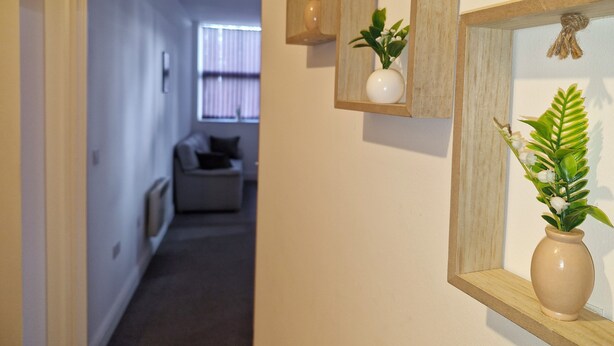 Ein Flur mit einer Tür zu einem Wohnbereich. Drei Holzrahmen-Spiegel mit Pflanzen hängen an der Wand.
