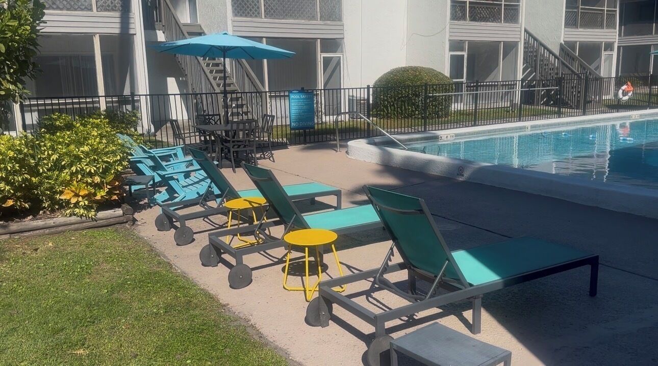 A poolside area with lounge chairs and tables, a pool, and a sign indicating no diving.