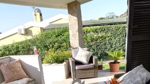 Ein möblierter Terrassenbereich mit Korbmöbeln, einer Tischplatte aus Glas und Topfpflanzen.