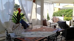 Eine überdachte Terrasse mit Esstisch, Stühlen und einem Blumentopf.