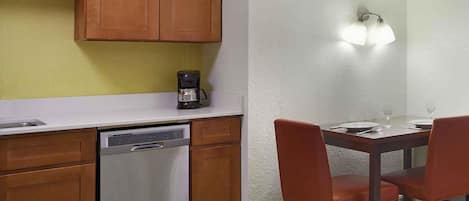 A compact kitchen with wooden cabinets, a dishwasher, a coffee maker, and a dining area with two chairs and a table.