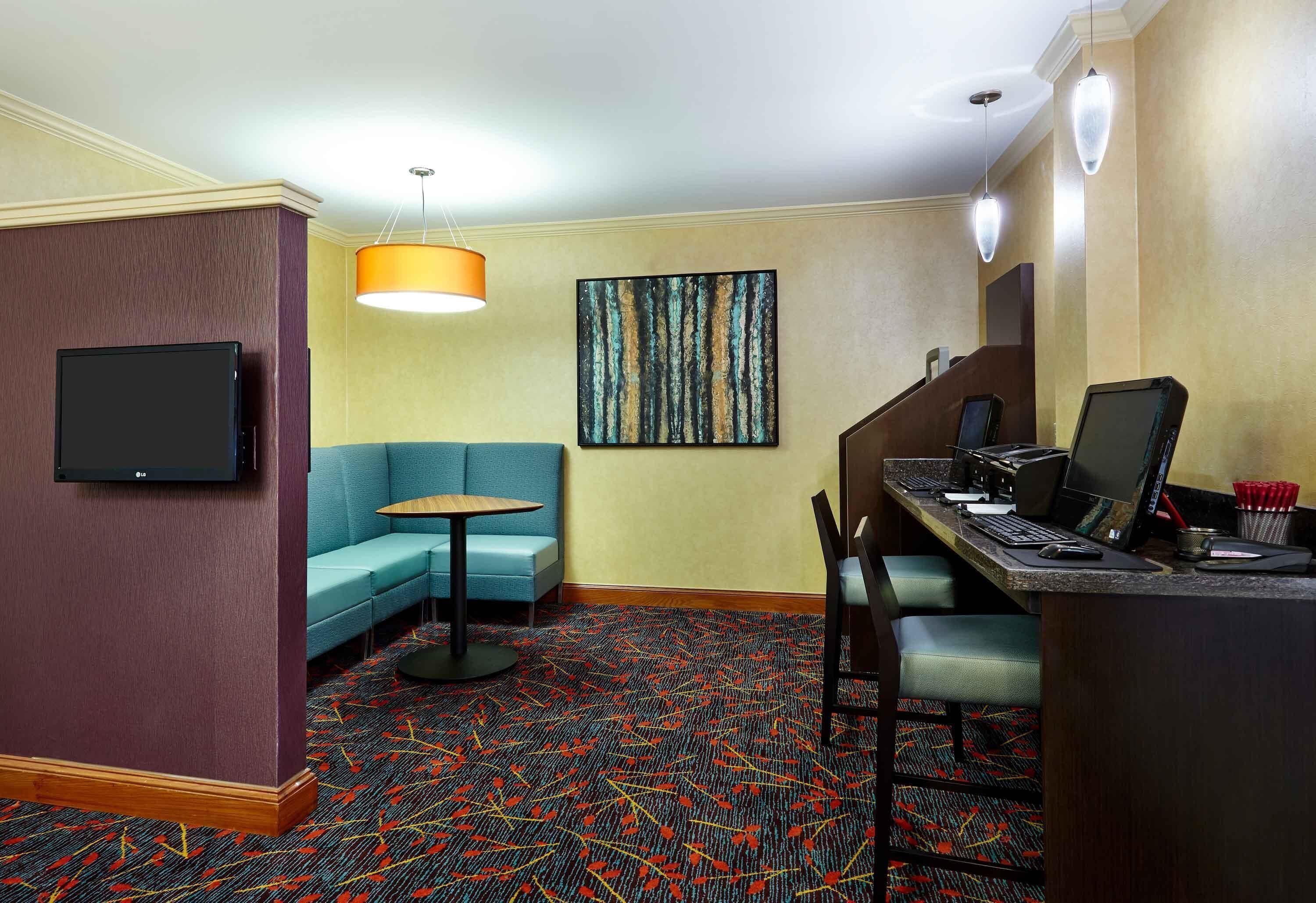 Ein Hotelzimmer mit Flachbildfernseher, einer Couch, einem Schreibtisch mit Computer und einem gemusterten Teppich.