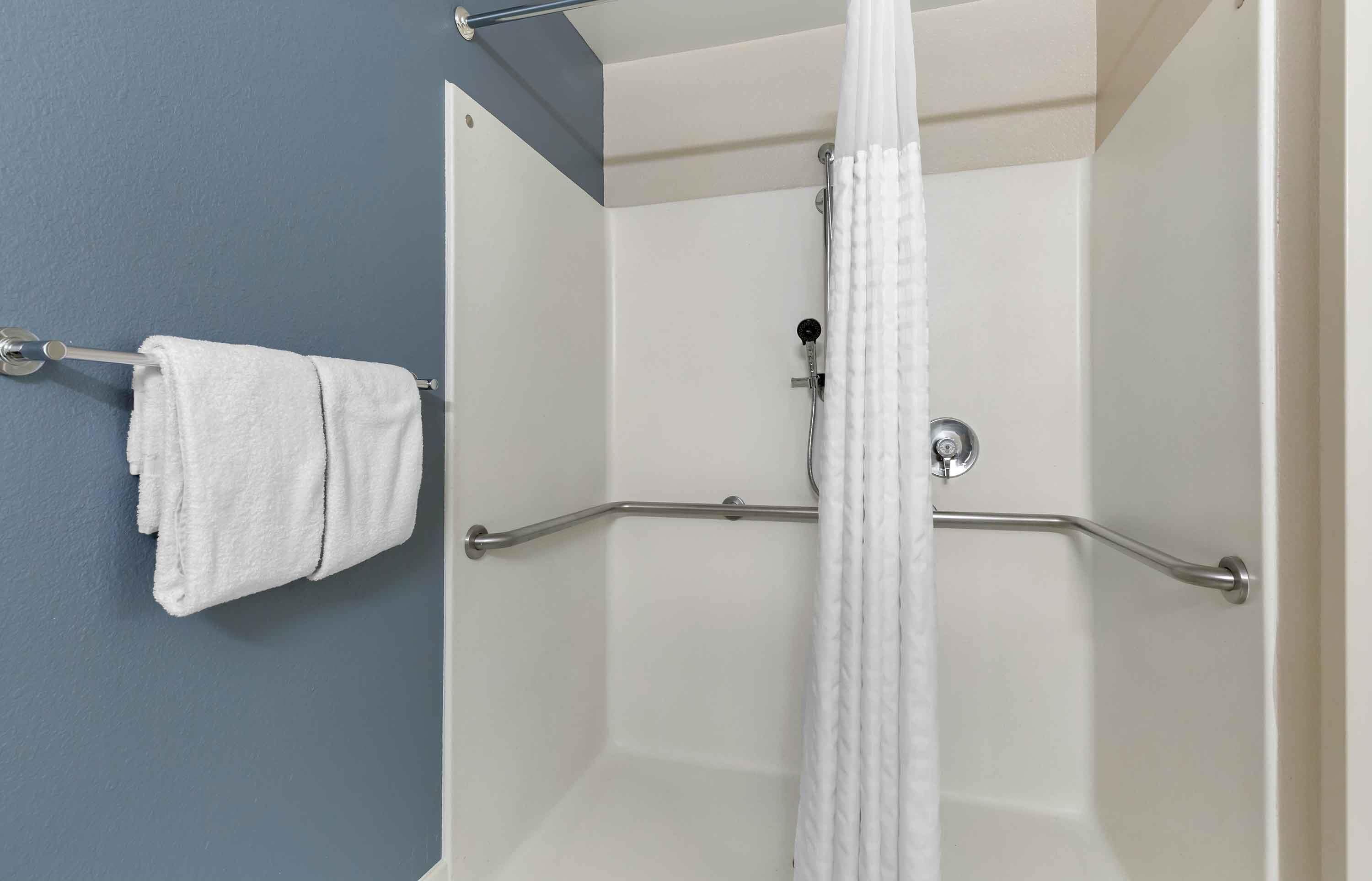 Eine Dusche mit weißem Vorhang, einem Handtuchhalter und einer Haltestange.