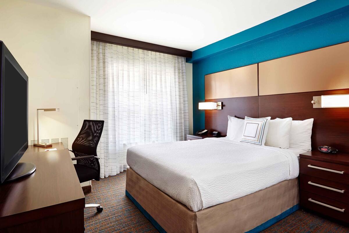 A hotel room with a bed, a desk, a television, a chair, and a nightstand.