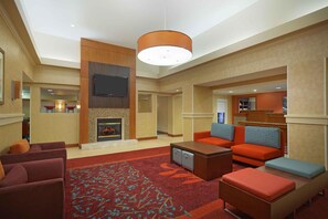 A hotel lobby with a fireplace, sofas, a television, and a patterned carpet. - Extended Stay America Suites - Houston - Galleria (Houston)