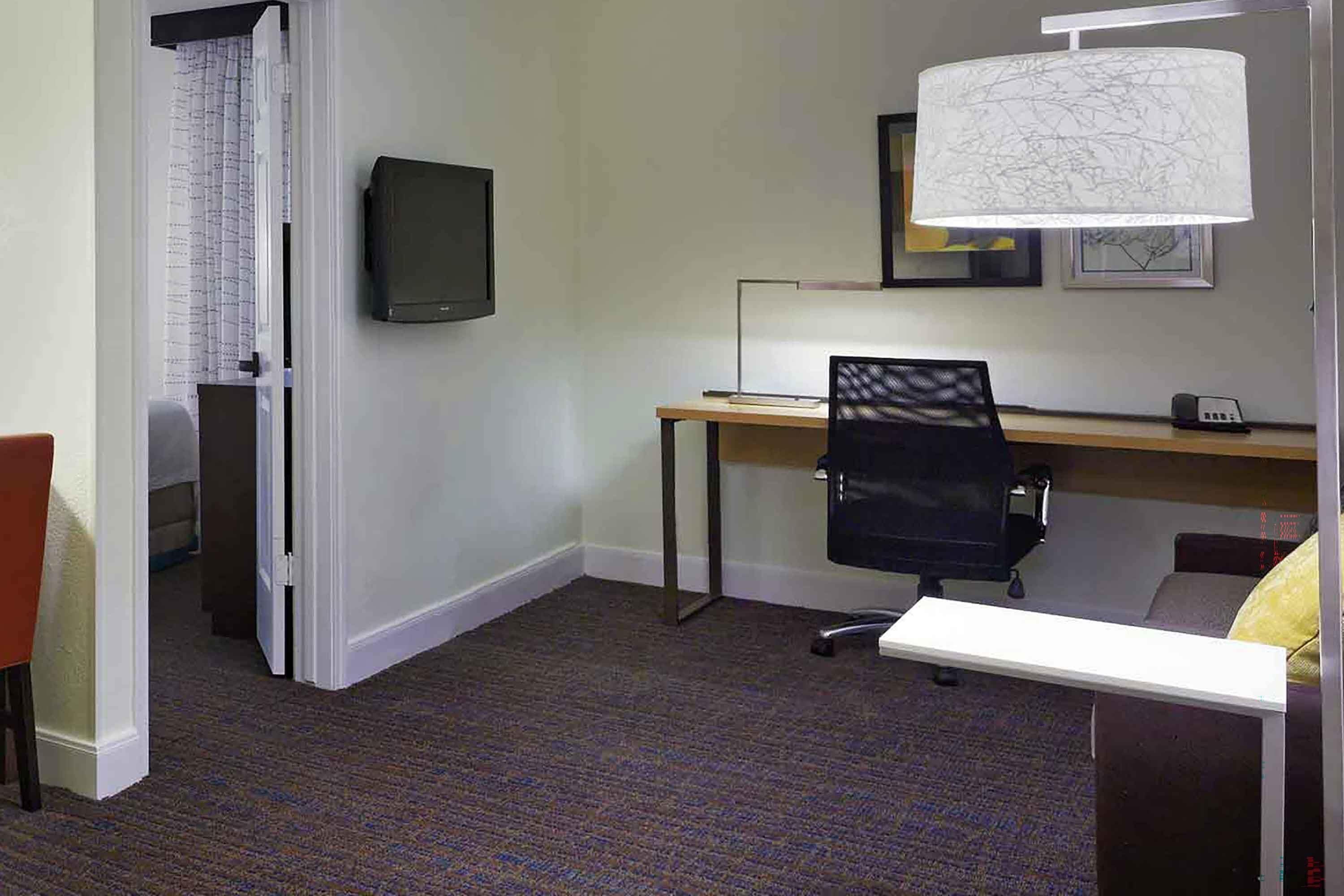 A hotel room with a desk, chair, and a television on the wall.