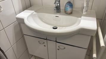 A bathroom with a white sink, a faucet, and a bottle of hand soap.