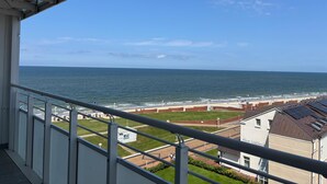 A balcony with a view of the sea and a beach area with buildings and a grassy field. - North Sea view "House An apartment 45" (Norderney)