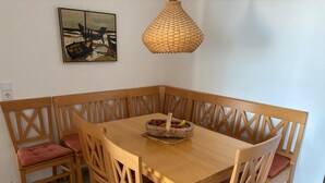 A dining area with a wooden table and chairs, a woven pendant light, and a painting on the wall. - North Sea view "House An apartment 45" (Norderney)