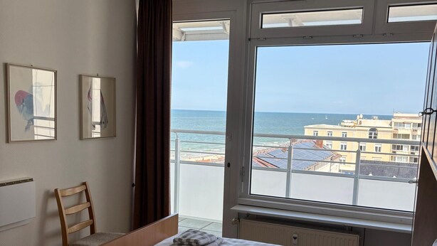 A hotel room with two beds, a window with a view of the sea, and a chair. - North Sea view "House An apartment 45" (Norderney)