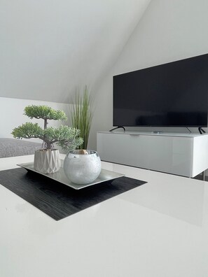 A modern living room with a flat-screen TV, a white entertainment unit, and two potted plants on a black tray. - Modern apartment close to Lake Cappenberg, 1-4 guests (Lünen)