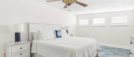 A bedroom with a bed, nightstand, lamp, ceiling fan, and windows.