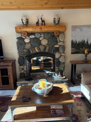 A cozy living room with a stone fireplace, a wooden coffee table with a bowl of snacks, a couch, and a painting on the wall. - Delightful 3-bedroom house in Truckee perfect for your getaway (Truckee)