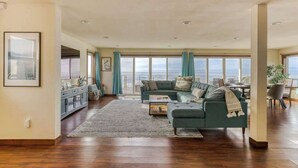 A spacious living room with a large window overlooking the ocean, a cozy sofa, and a wooden floor. - The Salt Life - Oceanfront escape Hot tub (Lincoln City)