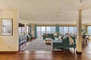 A spacious living room with a large window overlooking the ocean, a cozy sofa, and a wooden floor. - The Salt Life - Oceanfront escape Hot tub (Lincoln City)