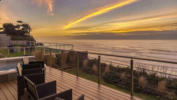 A deck with outdoor furniture overlooking a body of water during sunset. - The Salt Life - Oceanfront escape Hot tub (Lincoln City)