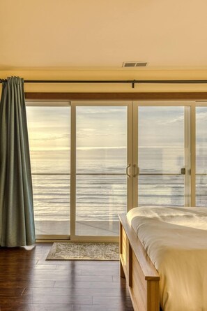 A bedroom with a large sliding glass door leading to a balcony, a bed, and a wooden floor. - The Salt Life - Oceanfront escape Hot tub (Lincoln City)