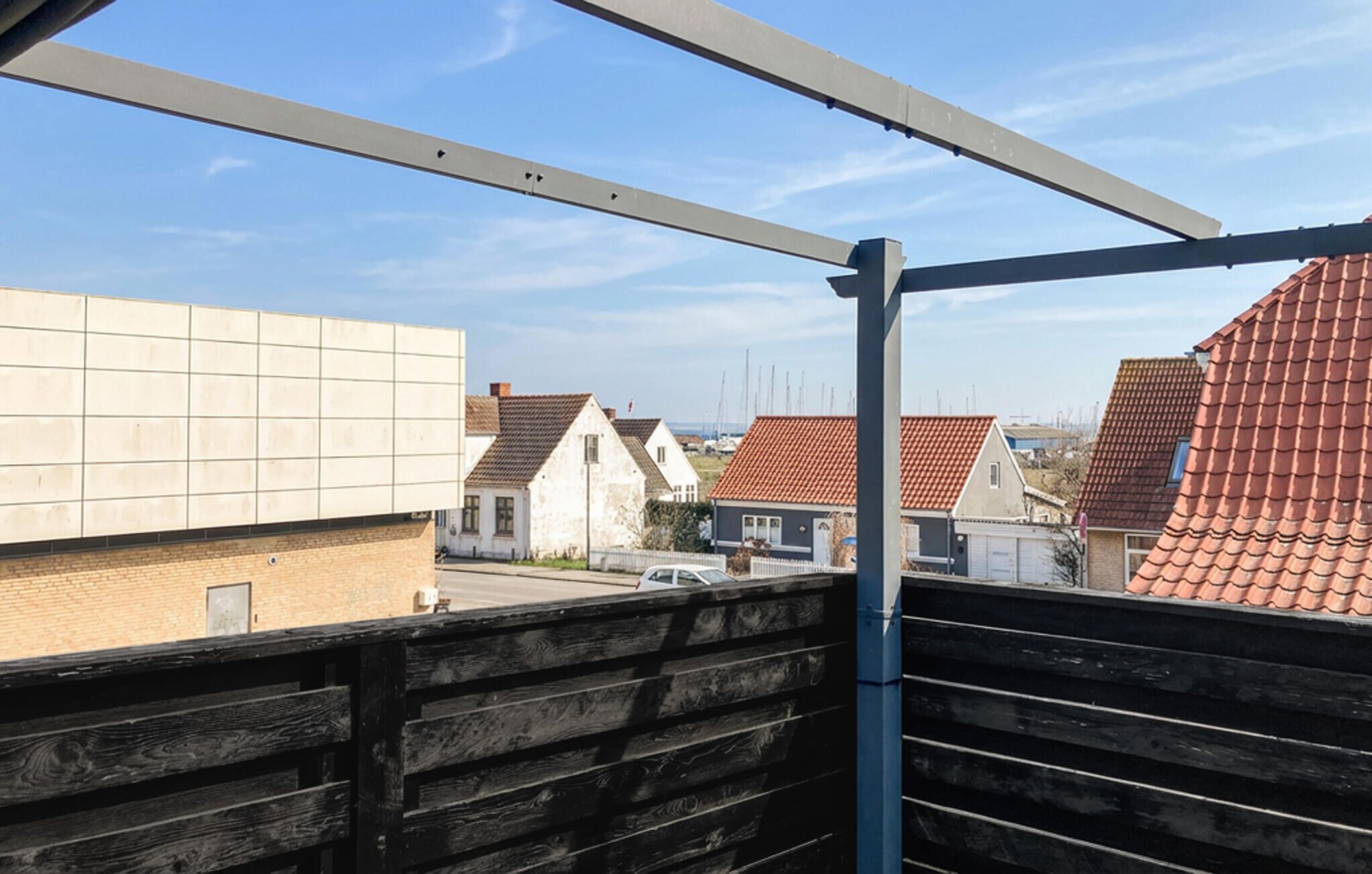 A view from a balcony with a metal railing, overlooking a residential area with houses and a clear sky.