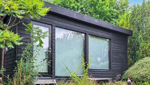 A modern, black wooden cabin with large glass windows, surrounded by lush greenery.