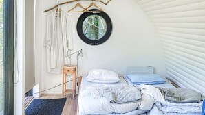 A cozy bedroom with a bed, a hanging light, a small wooden nightstand, and a window with a view.