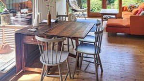 A wooden dining table with two chairs, a vase with flowers, and a view of the outdoors.