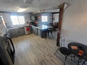 Una cocina con suelo de madera, un refrigerador, un lavamanos y una zona de comedor con mesa y sillas.