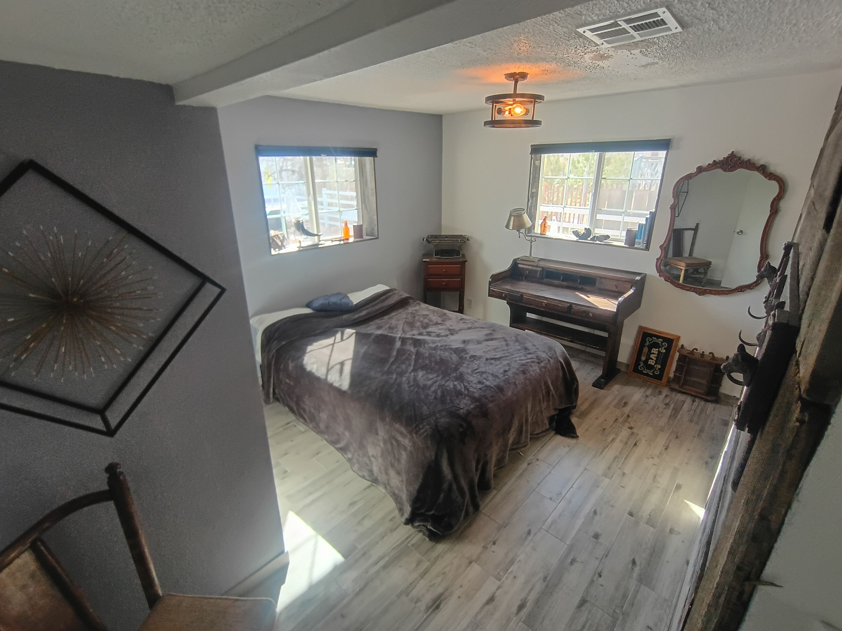 A bedroom with a bed, a desk, a mirror, and a window.