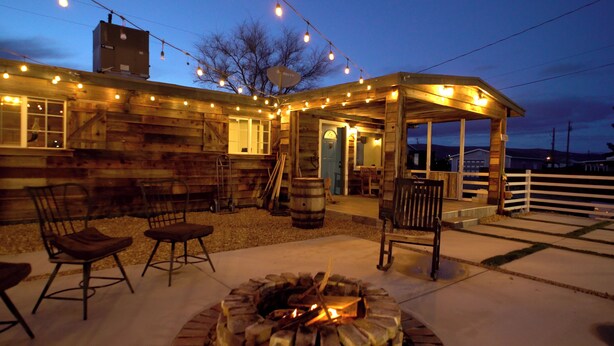 A rustic wooden building with a covered patio area featuring outdoor seating and a fire pit. - Haunted 3-bedroom Mining Cabin, only 8 miles from Death Valley Park - Beatty, NV (Beatty)