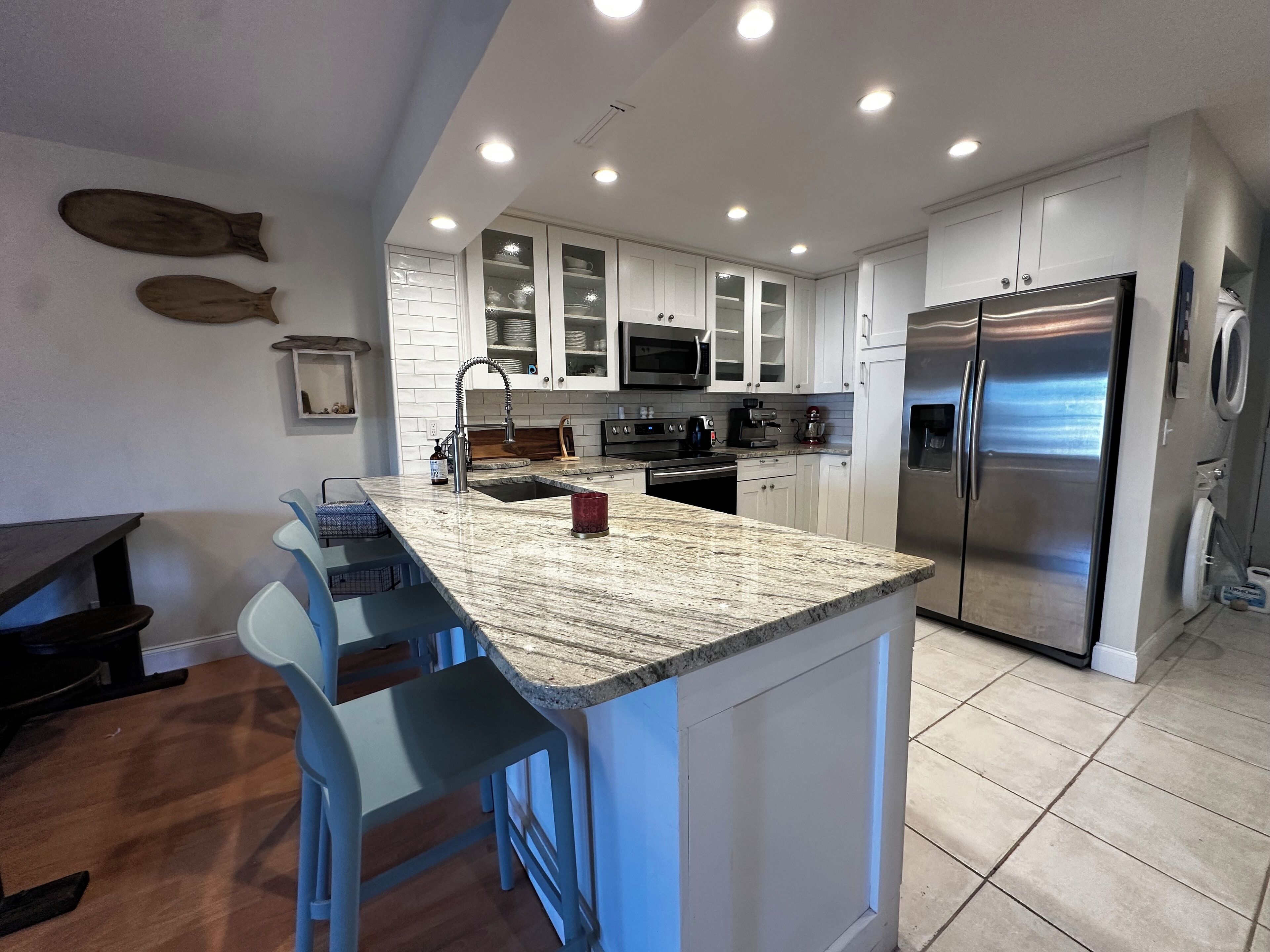 A modern kitchen with white cabinets, a granite countertop, stainless steel appliances, and a bar area with blue barstools.