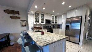 A modern kitchen with white cabinets, a granite countertop, stainless steel appliances, and a bar area with blue barstools. - 2-bedroom townhome in quaint Ponce Inlet, with direct private beach access! (Ponce Inlet)