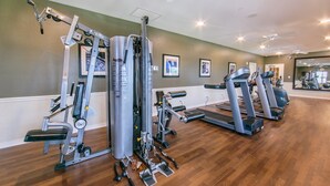 Un gimnasio con varias máquinas de ejercicio, una cinta de correr y un espejo que refleja los equipos.