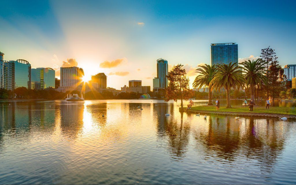 Une vue urbaine avec un plan d’eau reflétant les bâtiments et un coucher de soleil.