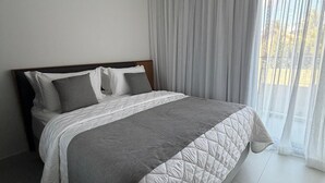 Camera d'hotel moderna con un letto grande, una testiera in legno e vista attraverso tende leggere.
