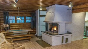 A cozy cabin interior with a wooden ceiling, a fireplace, a dining table, and a cushioned chair. - Hännänpää by Interhome (Vihti)