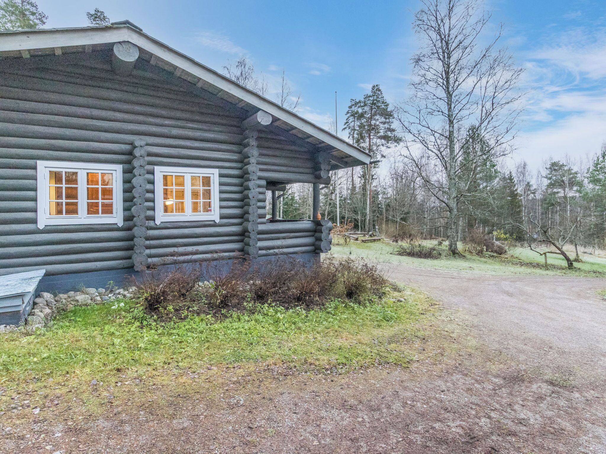 En timmerstuga med två fönster, en veranda och en grusgång som leder fram till den.