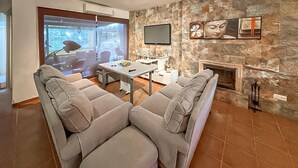 Una sala de estar moderna con una pared de piedra, una chimenea, un televisor de pantalla plana y un comedor con mesa y sillas.