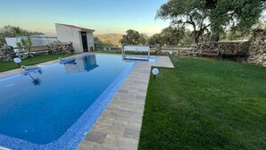 Una piscina rectangular con borde de azulejos, rodeada por una terraza de madera y una zona de césped.