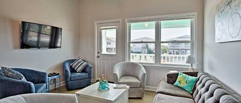 A living room with a large window, a flat-screen TV, and a sofa set.