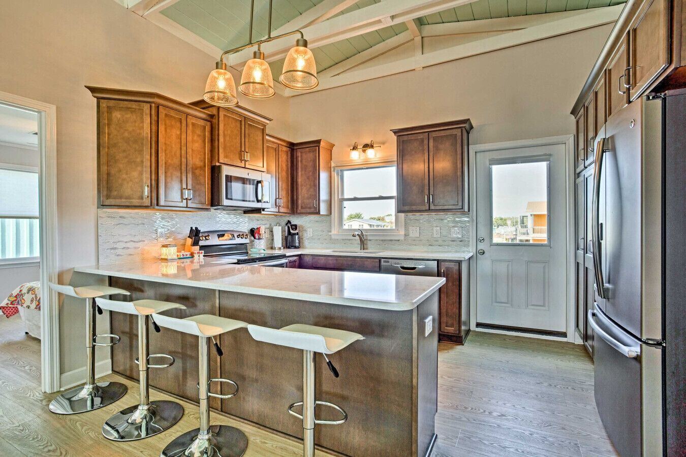 A modern kitchen with a large island, bar stools, stainless steel appliances, and wooden cabinets.